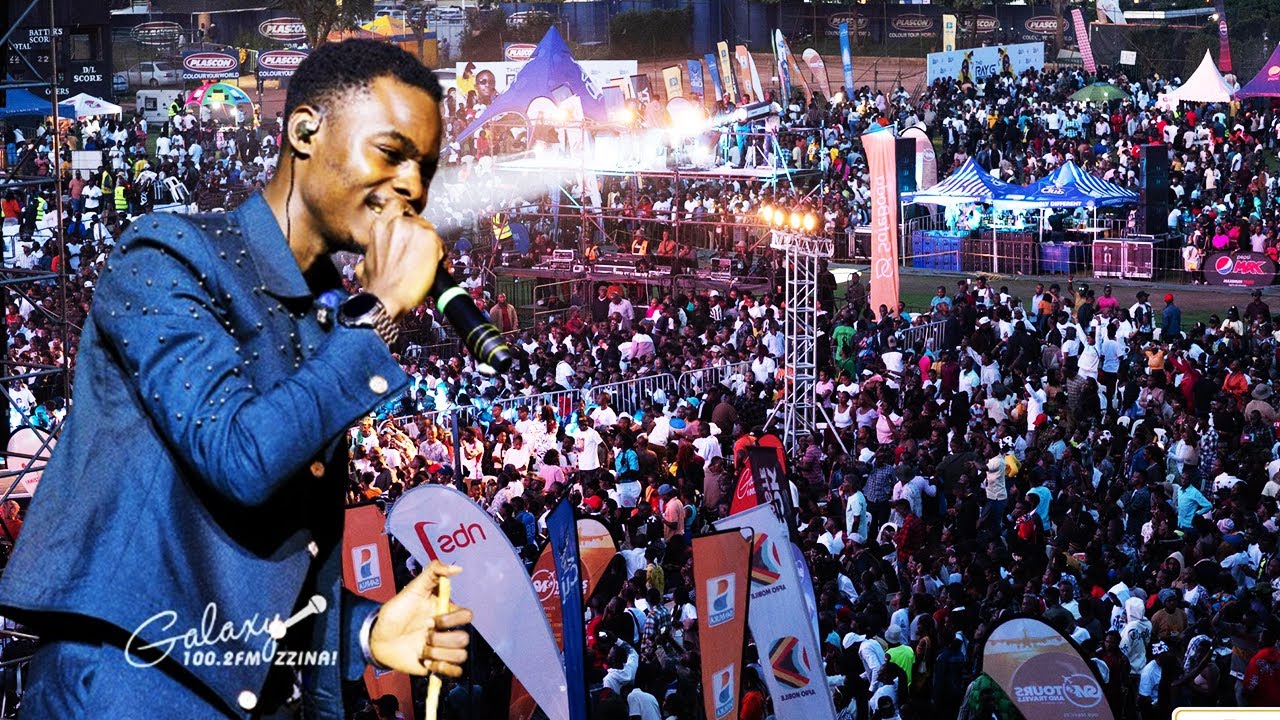 Muhairwe Reagan performing on stage with a microphone, surrounded by cheering fans.