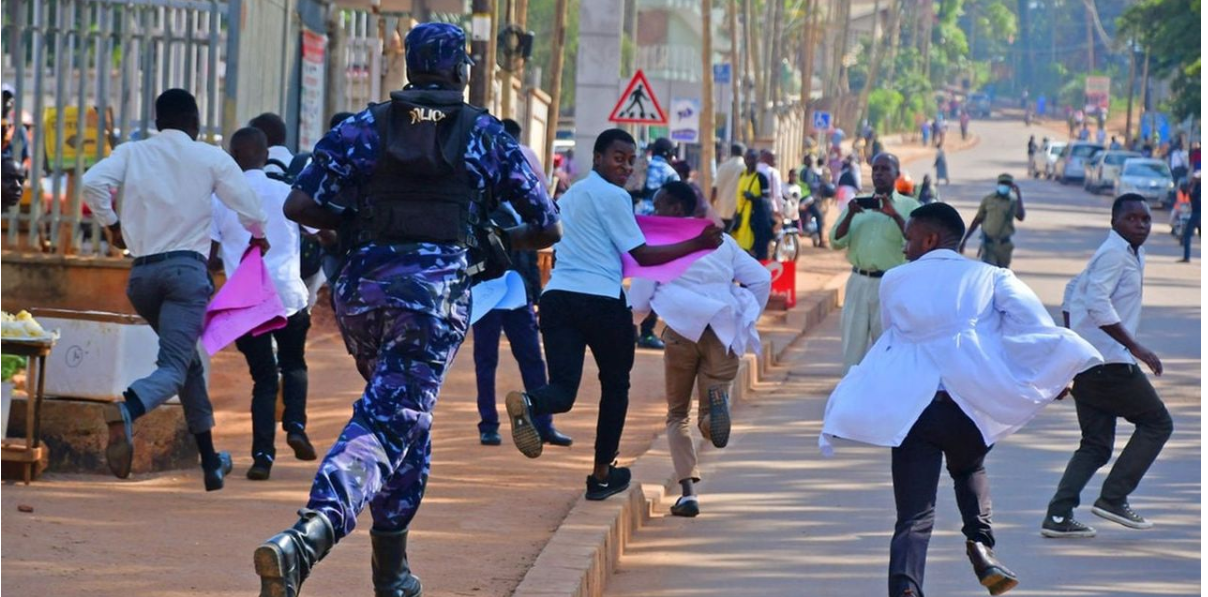 A group of Ugandan medical interns, holding protest signs, gather in front of a government building, demanding deployment and a supplementary budget from the Ministry of Health. The image captures their frustration and determination as they prepare to take their concerns to Parliament's regional sessions in Gulu City